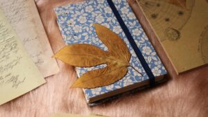 Flat lay con materiales de junk journal: cuaderno hecho a mano, papeles vintage, hojas secas y herramientas