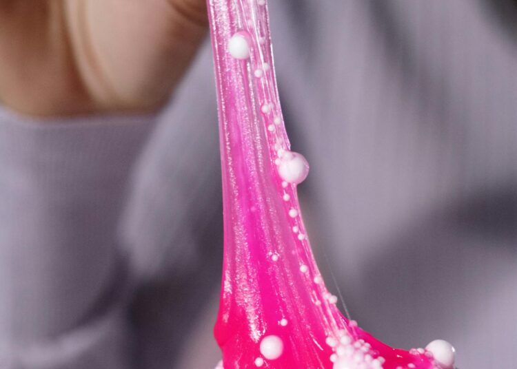 Manos estirando slime casero de color rosa brillante, demostrando la textura perfecta del slime sin bórax para niños