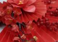 Abanico artesanal decorado con flores rojas sobre fondo cálido, idea de abanicos de papel