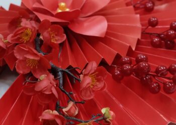 Abanico artesanal decorado con flores rojas sobre fondo cálido, idea de abanicos de papel