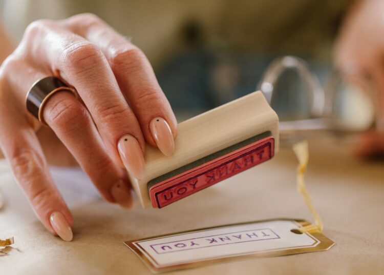 Manos estampando una tarjeta con sellos caseros sobre una mesa de manualidades