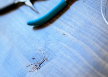 Alicates y herrajes de bisutería sobre una mesa de madera junto a alambre y piezas metálicas