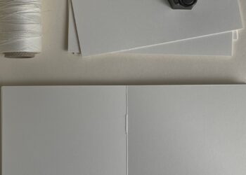 Manos cosiendo cuadernillos de papel con hilo en un proyecto de encuadernación artesanal