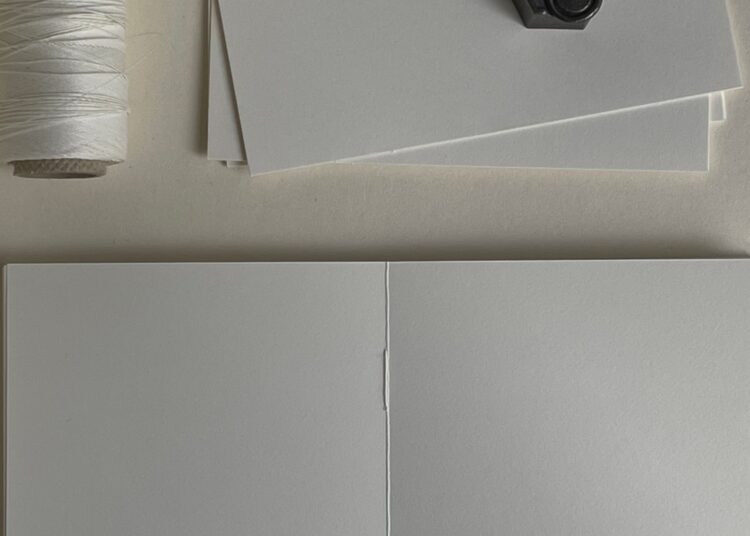 Manos cosiendo cuadernillos de papel con hilo en un proyecto de encuadernación artesanal