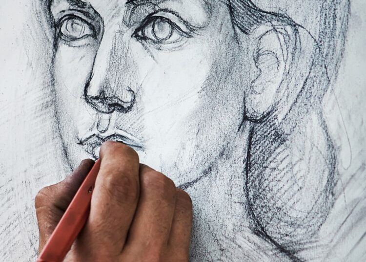 Primer plano de una mano dibujando a lápiz en un cuaderno, ejemplo de cómo dibujar manos paso a paso