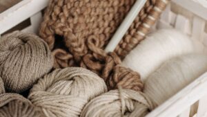 Ovillos de distintos tipos de lana para tejer en una cesta junto a unas agujas de madera