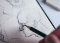 Mano dibujando ojos a lápiz sobre papel blanco en un cuaderno de bocetos