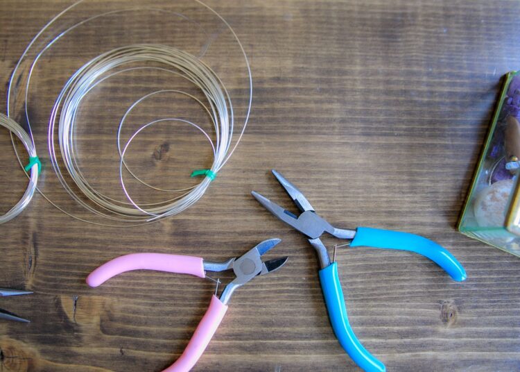 Pinzas y bobinas de alambre sobre una mesa para hacer joyas con alambre paso a paso