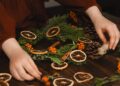 Coronas de Navidad DIY: manos montando una corona con ramas verdes y cinta roja