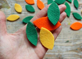 Manos sosteniendo hojas de fieltro de colores sobre madera para manualidades con fieltro