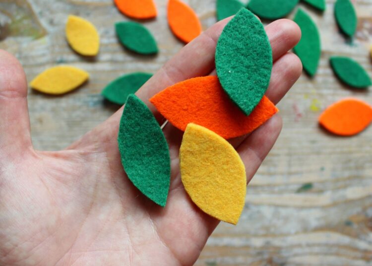 Manos sosteniendo hojas de fieltro de colores sobre madera para manualidades con fieltro