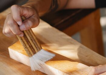 Manos aplicando barniz con brocha sobre una tabla de madera al barnizar madera en un taller