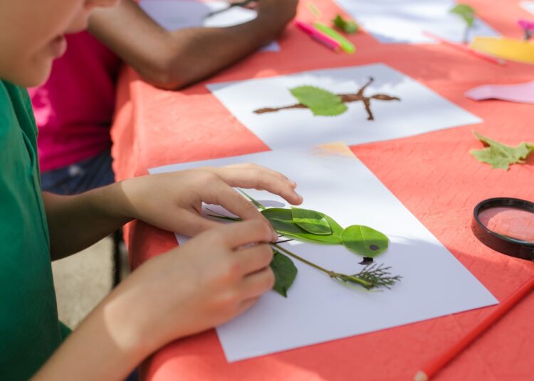 Niño haciendo manualidades de otoño con hojas secas de colores sobre una mesa