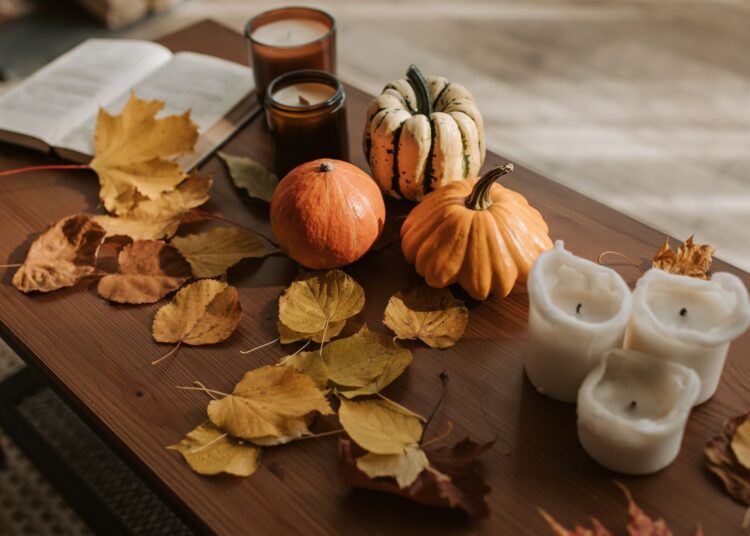 Decoración de otoño sobre una mesa con calabazas, velas encendidas y hojas secas en tonos cálidos