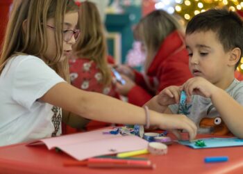 Niños haciendo manualidades de Navidad en una mesa decorada